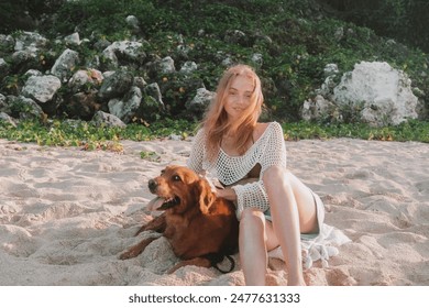 Young redhead woman sitting on a sandy beach near the ocean with a golden retriever and smiling. A woman gently strokes her dog and hugs it. Walking with your pet at dawn on a deserted beach. - Powered by Shutterstock