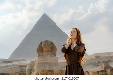 Young redhead woman standing in front of the Great Sphinx of Giza with the amazing Pyramid at the back. Valley of the Kings, Cairo, Egypt. Blurred background