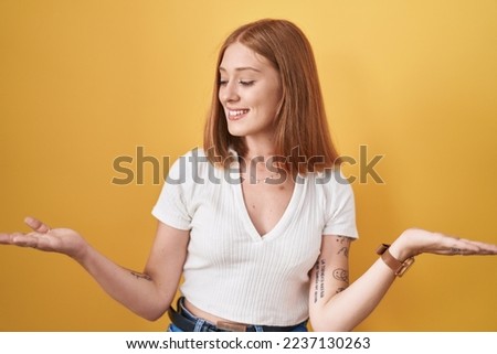 Young redhead woman standing over yellow background smiling showing both hands open palms, presenting and advertising comparison and balance 