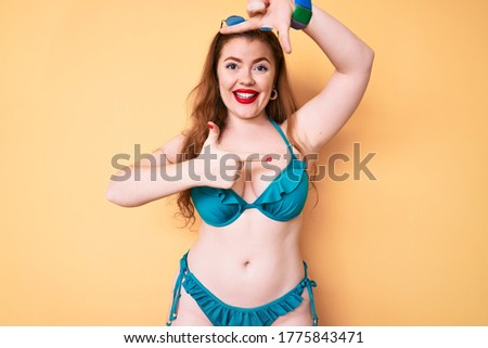 Young redhead woman wearing bikini smiling making frame with hands and fingers with happy face. creativity and photography concept. 