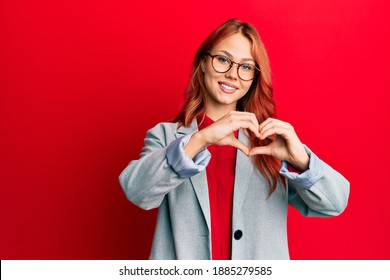 Young Redhead Woman Wearing Business Jacket And Glasses Smiling In Love Showing Heart Symbol And Shape With Hands. Romantic Concept. 