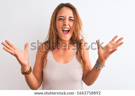 Young redhead woman wearing casual t-shirt stading over white isolated background celebrating crazy and amazed for success with arms raised and open eyes screaming excited. Winner concept
