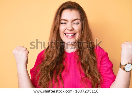 Young redhead woman wearing casual clothes celebrating surprised and amazed for success with arms raised and eyes closed 