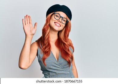 Young Redhead Woman Wearing Fashion French Look With Beret Waiving Saying Hello Happy And Smiling, Friendly Welcome Gesture 