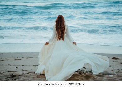 Mulher ruiva jovem em branco vestido vintage nupcial andando à beira-mar. Meditação