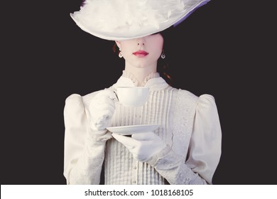 Junge Rotkopffrau in weißer, viktorianischer Kleidung mit Tasse Tee auf schwarzem Hintergrund.