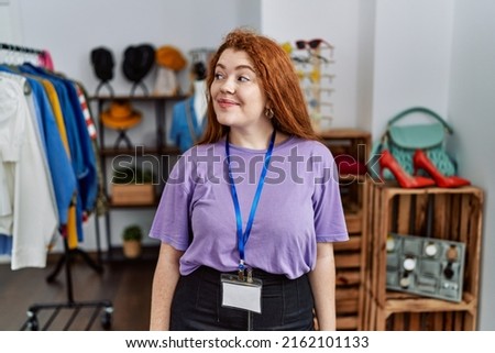 Young redhead woman working as manager at retail boutique smiling looking to the side and staring away thinking. 