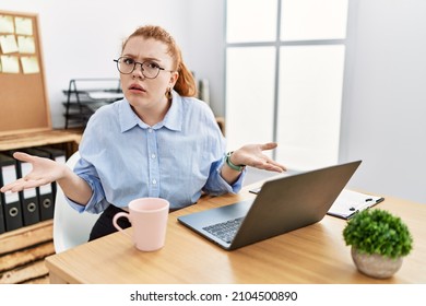 Young Redhead Woman Working At The Office Using Computer Laptop Clueless And Confused With Open Arms, No Idea Concept. 