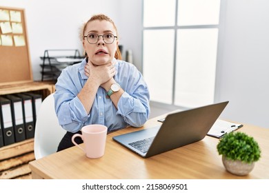Young redhead woman working at the office using computer laptop shouting suffocate because painful strangle. health problem. asphyxiate and suicide concept. 