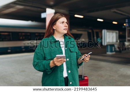Young refugee redhhead woman crying and waiting train on station platform, she lost and using smart phone. Railroad transport concept, Traveler.