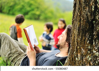 Young relaxed father reading book and children playing around - Powered by Shutterstock