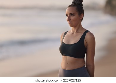 Young relaxed woman in activewear warming up while working out on beach with ocean on blurred background - Shutterstock ID 2257027125