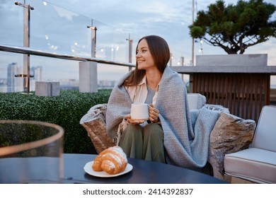 Young relaxed woman drinking coffee spending cozy evening at rooftop cafe - Powered by Shutterstock