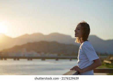 Young relaxed woman on terrace enjoying the sunset landscape with mountains over sea