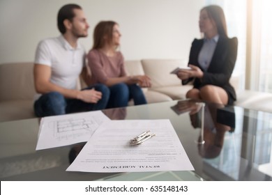 Young Renters Couple Sitting On Couch Discussing Renting Apartment With Real Estate Agent, Focus On Rental Agreement And Keys, Property Lease Contract. Looking For Accommodation, Long-term Tenancy