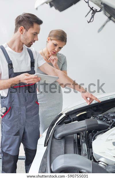 Young repair worker explaining car engine to\
worried customer in\
workshop