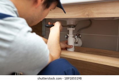 The young repairer is fixing sink in the bathroom