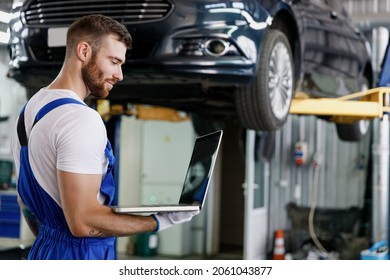 Young repairman professional technician mechanic man 20s in blue overalls t-shirt use hold laptop pc computer stand near car lift check technical condition work in vehicle repair shop workshop indoor - Powered by Shutterstock