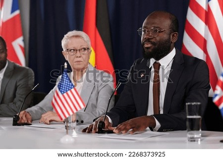Young representative of USA making speech at political summit or conference while speaking in microphone in front of audience