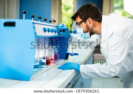 Young researcher with protective goggles checking test tubes in flocculator at the laboratory