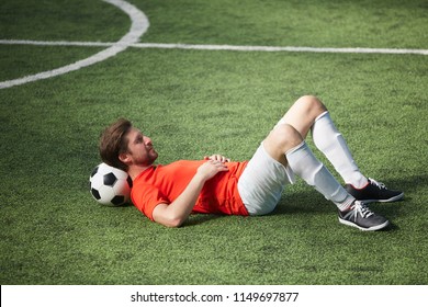 Young restful footballer lying on green field with soccer ball behind his neck - Powered by Shutterstock