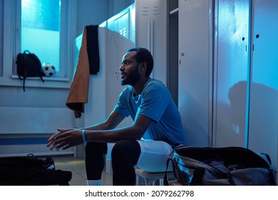 Young Restful Professional Soccer Player In Sports Uniform Sitting Against Lockers In Changing Room