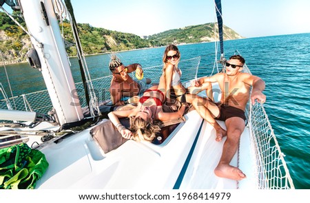 Young rich friends chilling on sailboat at sea trip - Guys and girls having summer fun together at sail boat party day - Luxury excursion concept on warm vivid filter with dutch angle composition