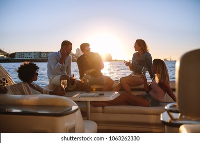 Young rich friends drinking wine and beers in boat party during sunset. Group of young people partying on yacht.