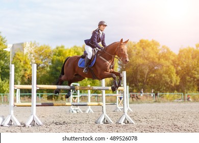 Young rider girl performing jump at horse show jumping competition. Equestrian sport background