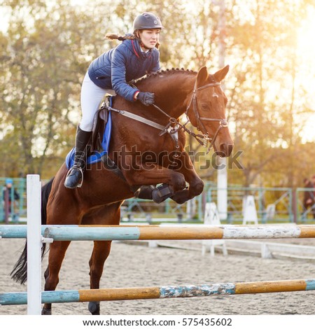 Young rider girl at show jumping. Horserider jumps over hurdle