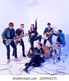 Young Rock Band Of Six People Emotionally Playing And Singing On A White Background With Blue Light Around