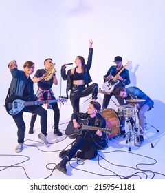 Young Rock Band Of Six People Emotionally Playing And Singing On A White Background With Blue Light Around