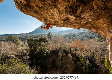 A young rock climber on an overhanging cliff. The climber climbs the rock. The girl is engaged in sports climbing. Sports in nature. - Powered by Shutterstock