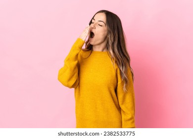 Young Romanian woman isolated on pink background yawning and covering wide open mouth with hand