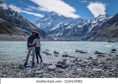 A young romantic couple admiring the beautiful scenery of mount cook in New Zealand. The rocky shore, stunning snow mountain and the clear sky create a perfect background or wallpaper.