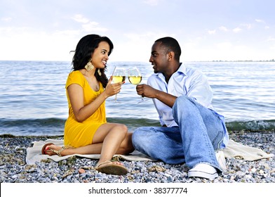 Young romantic couple celebrating with wine at the beach looking at each other
