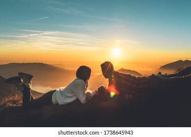 A Young Romantic Couple Enjoy A Beautiful View Of The Sun Setting Over The Mountains In Italy.