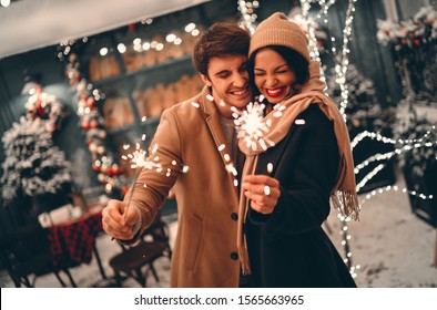 Young romantic couple having fun outdoors in winter before Christmas with sparklers in hands.Enjoying spending time together in New Year Eve.Two lovers are hugging and kissing in Saint Valentine's day - Powered by Shutterstock