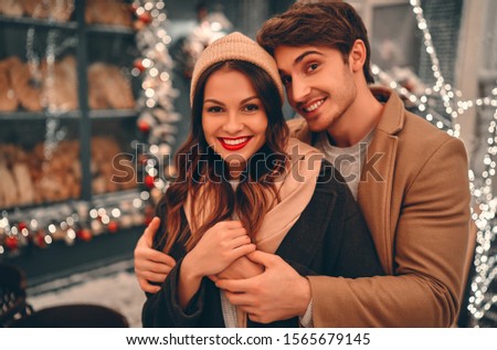 Young romantic couple is having fun outdoors in winter before Christmas. Enjoying spending time together in New Year Eve. Two lovers are hugging and kissing in Saint Valentine's Day.