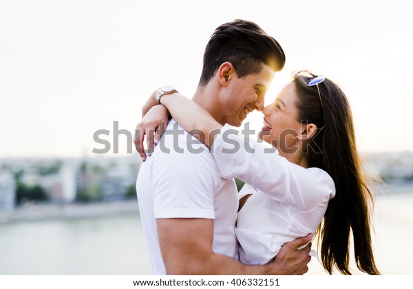 美しい夕焼けの中で抱き合いキスをしようとする若いロマンチックな夫婦 の写真素材 今すぐ編集