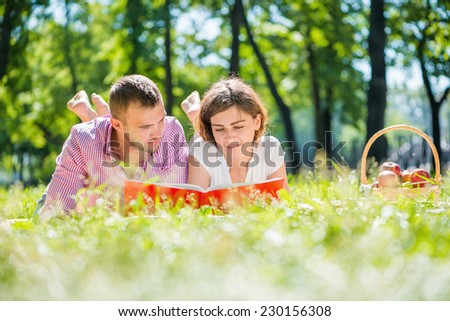 Young romantic couple lying in park and reading book
