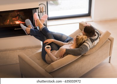 Young romantic couple sitting on sofa in front of fireplace at home, looking at each other, talking and drinking coffee at autumn day - Powered by Shutterstock