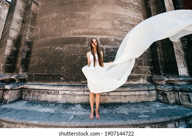 Young romantic elegant girl in long white flowy dress posing over stone ancient wall