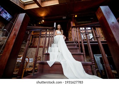 Young romantic elegant girl in long white flowy dress posing on the stairs indoor