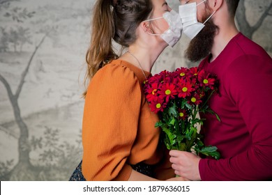 Young romantic loving couple wearing a protective face mask for coronavirus and kissing, holding bouquet of flowers. Valentines day and Covid-19 concept romance