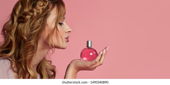 Young romantic tender girl with long curly hair in a lilac dress holds in her hand a bottle of pink perfume.
