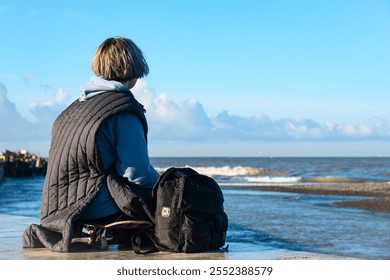 A young romantic woman sits on the pier and looks at the surf, tired of skateboarding - Powered by Shutterstock