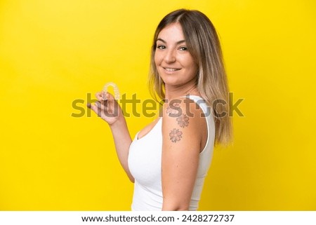Young Rumanian woman holding envisaging isolated on yellow background smiling a lot