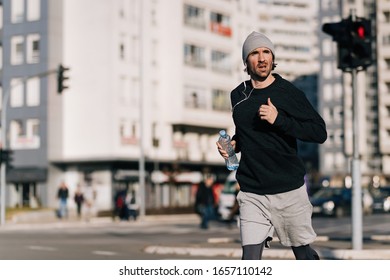 Young Runner Carrying Bottle Of Water While Jogging On The Street. 