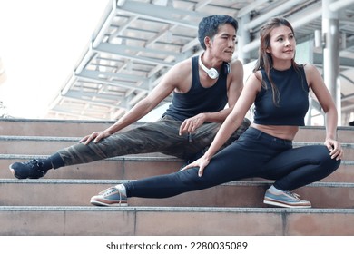 Young runner man and woman lover doing exercise together outside, partner buddy runner stretching body at staircase before run outdoor, two Asian jogger athlete training and doing workout in city
